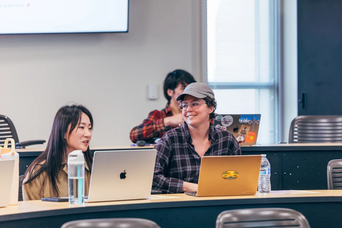 Two participants talk and smile across their laptops during the hands-on portion of an AI Kitchen session.