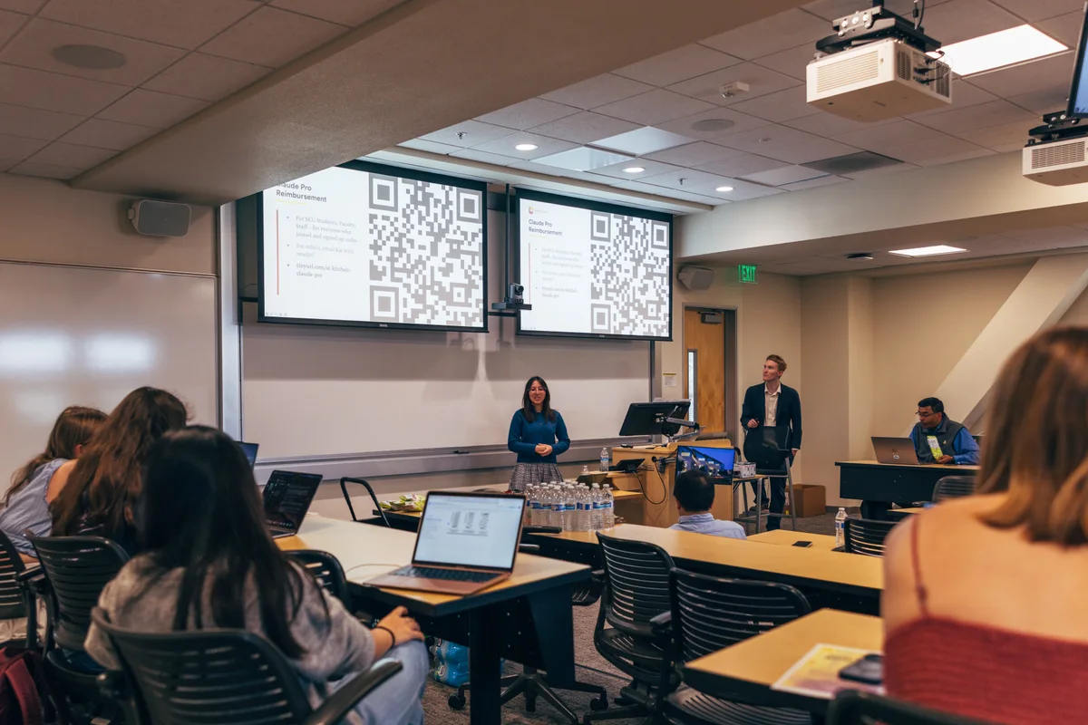 A room of participants watches presenters demonstrate a workflow at the front of AI Kitchen.