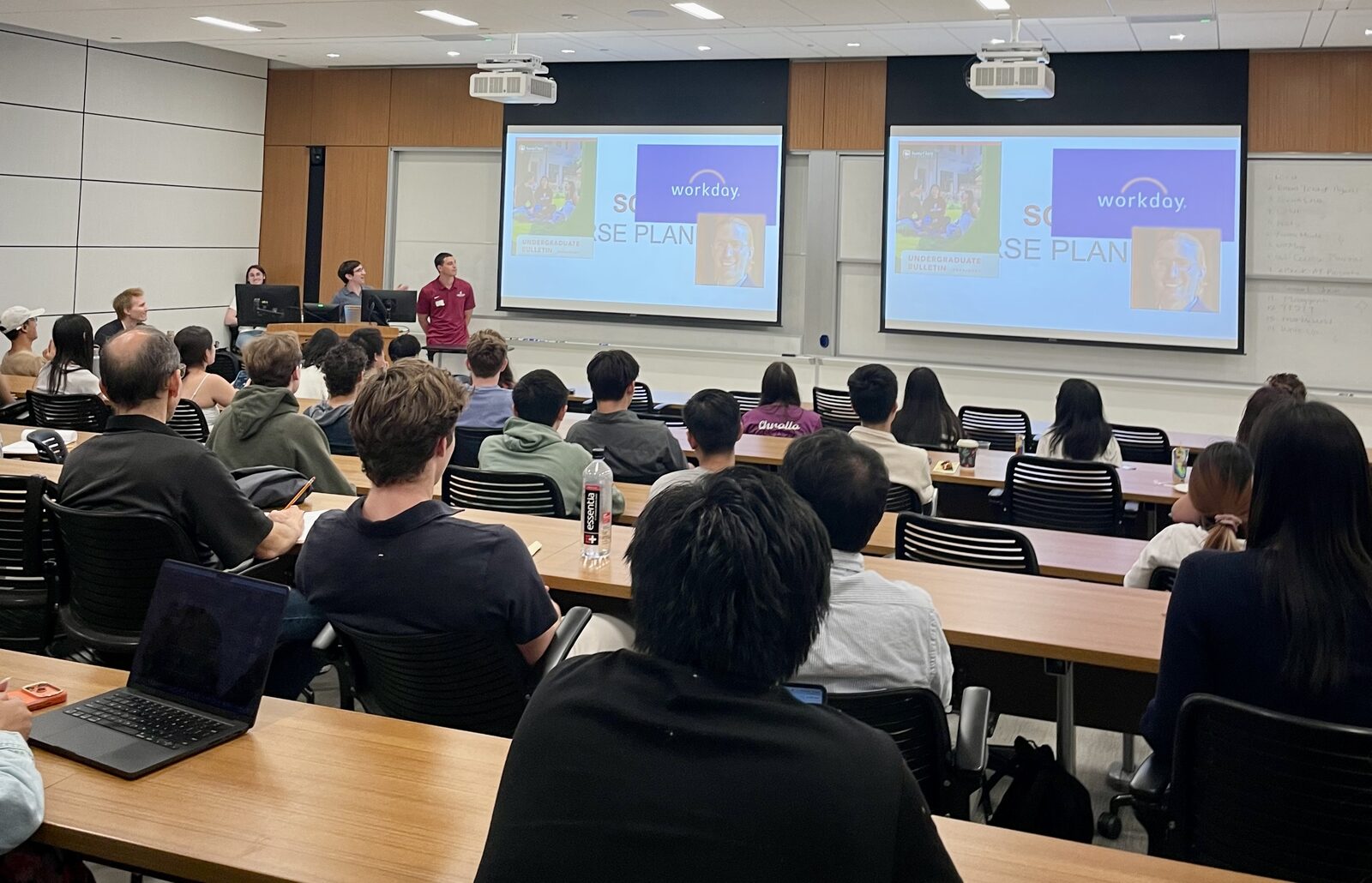 A team pitches on the dual screens to a seated audience in lecture hall SCDI 1302.