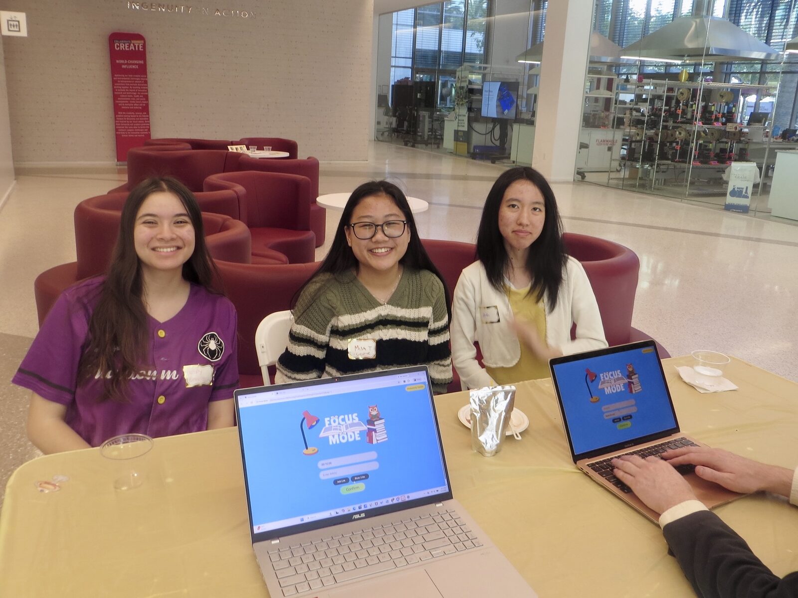 Three students smile at their demo table with Focus Mode open on two laptops.