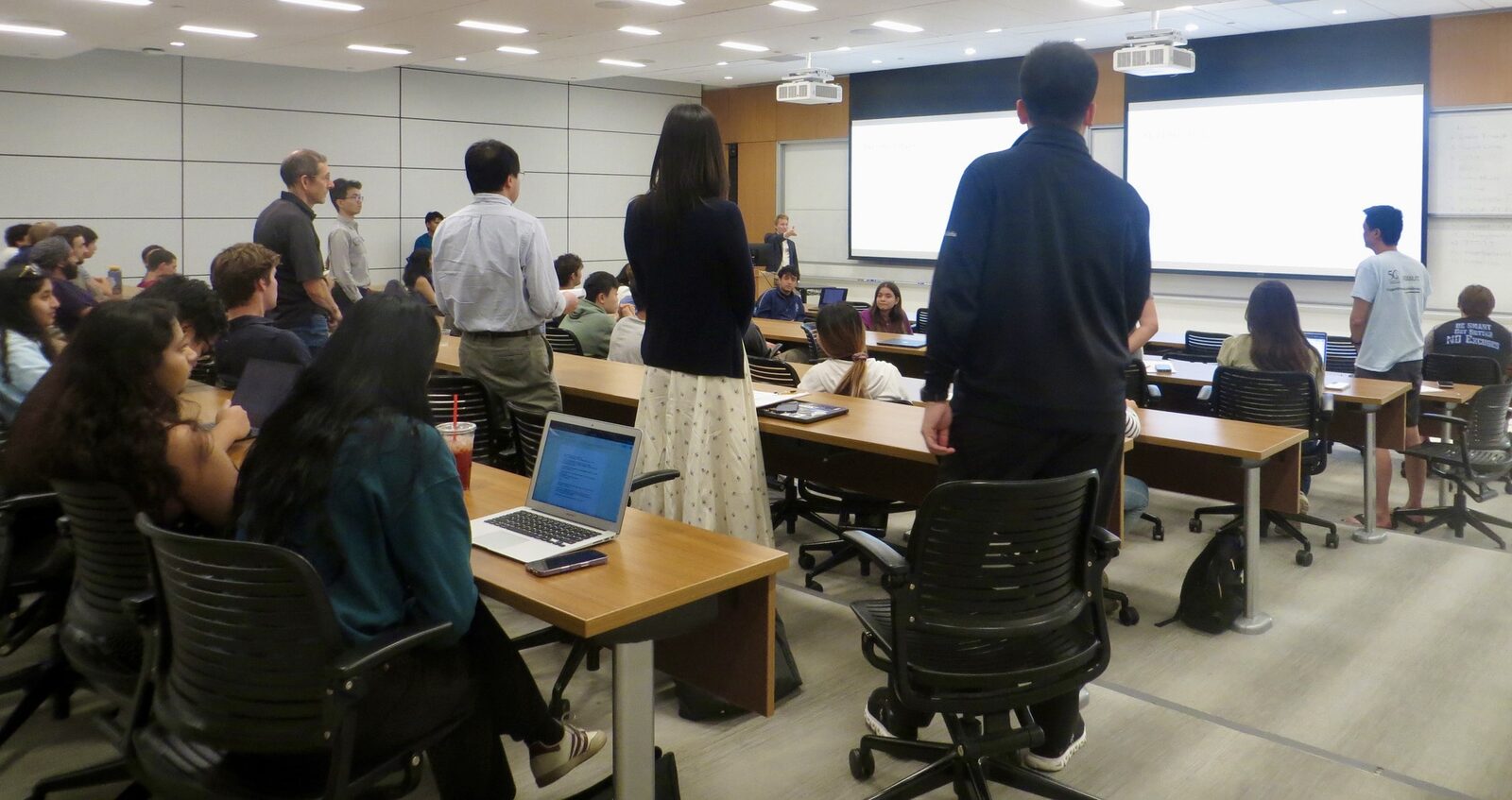 Judges and guests stand along the side of the lecture hall watching the pitches.