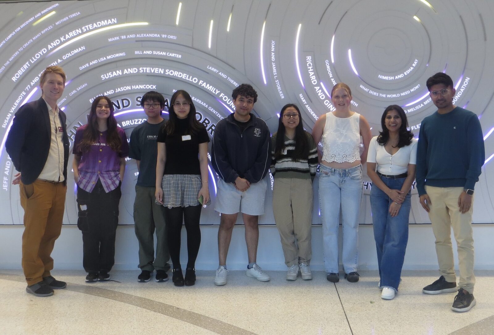 The AI Kitchen organizing team poses in front of the lobby's lit donor wall.