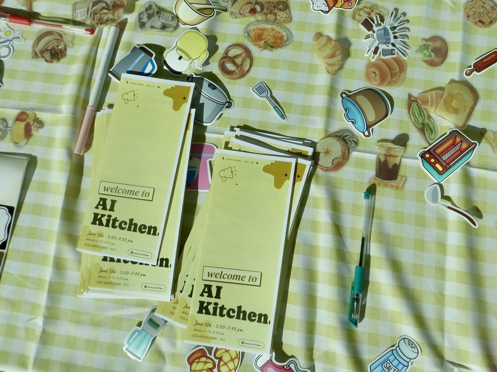 Welcome to AI Kitchen program cards and stickers on a gingham tablecloth.